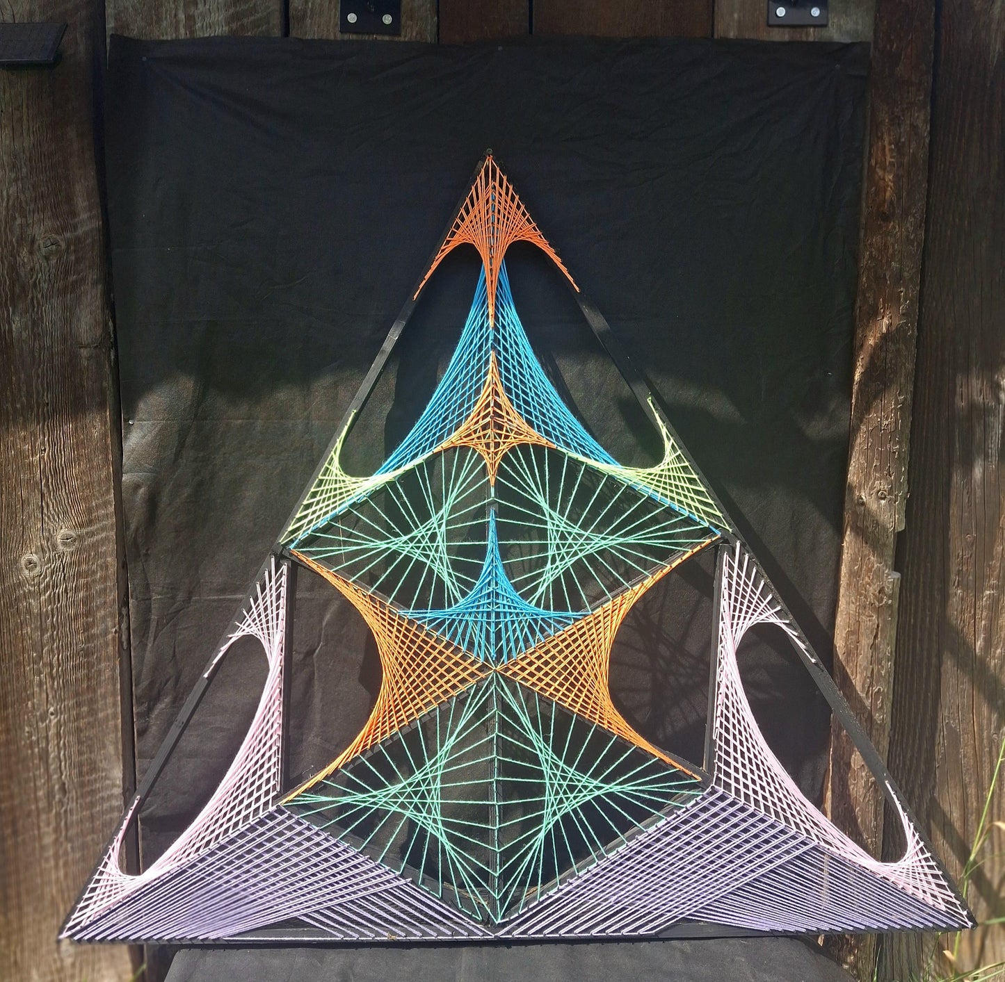 Geometric string art wall sculpture Aliens Gate by Psybell displayed outdoors against dark fabric background