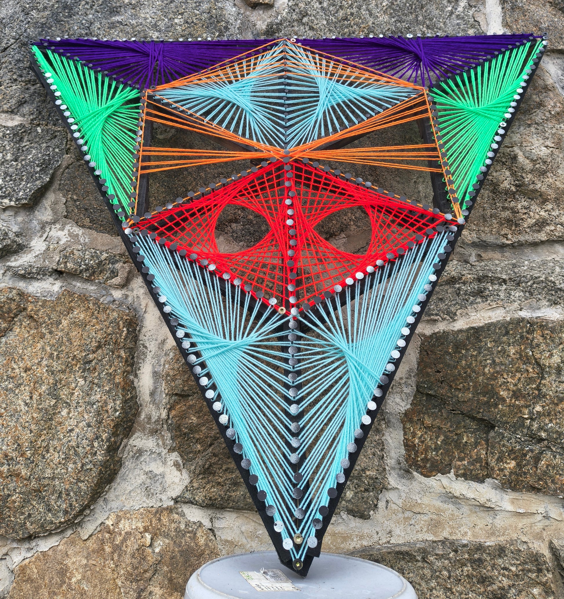 Alien’s Sentinel handmade string art photographed in daylight, geometric alien-inspired design made with colored threads on wooden base, detailed modern wall art by Psybell