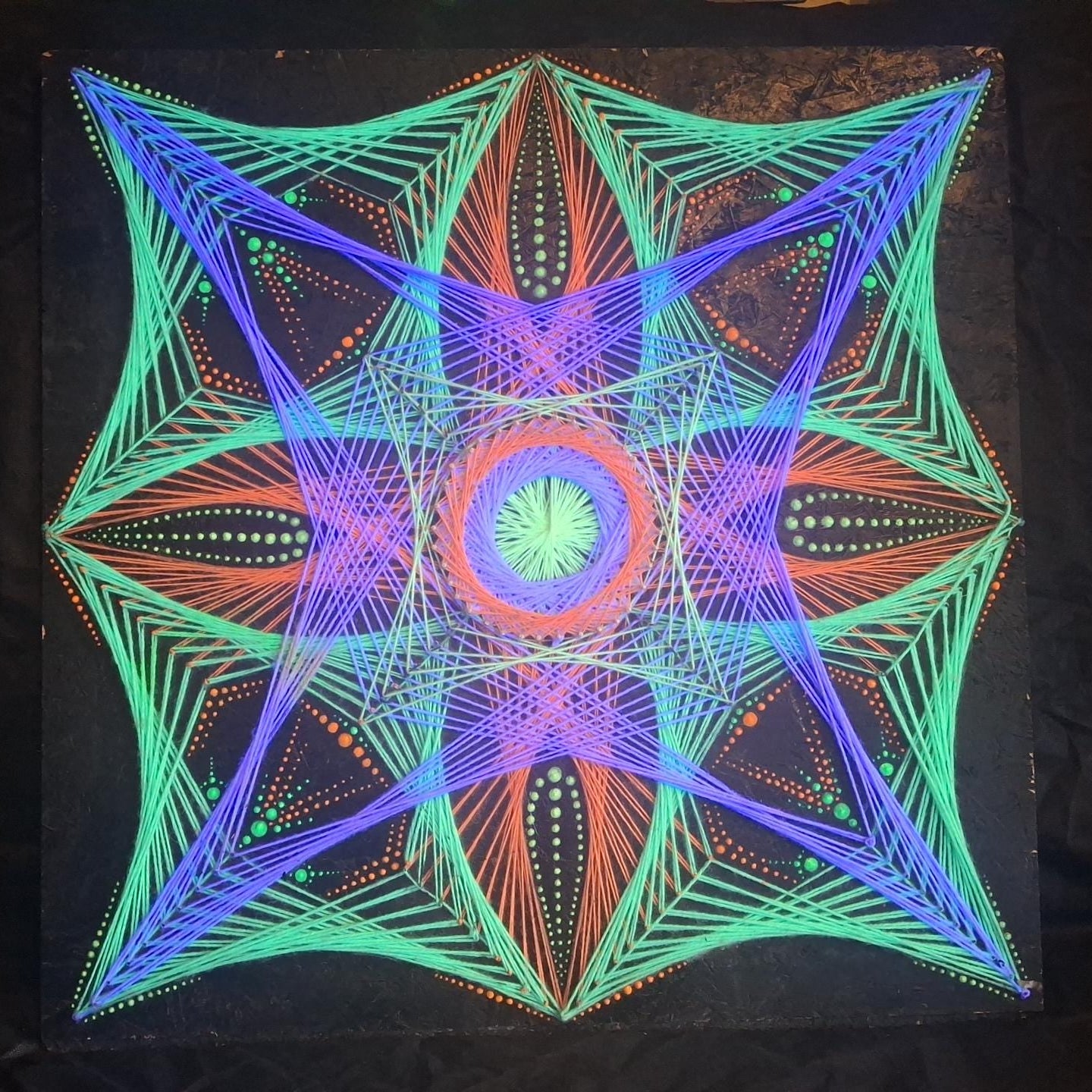 handmade UV reactive string art mandala “Aura Flow” glowing under ultraviolet light, geometric dotted pattern created with nails and threads on wooden board, psychedelic wall art by Psybell