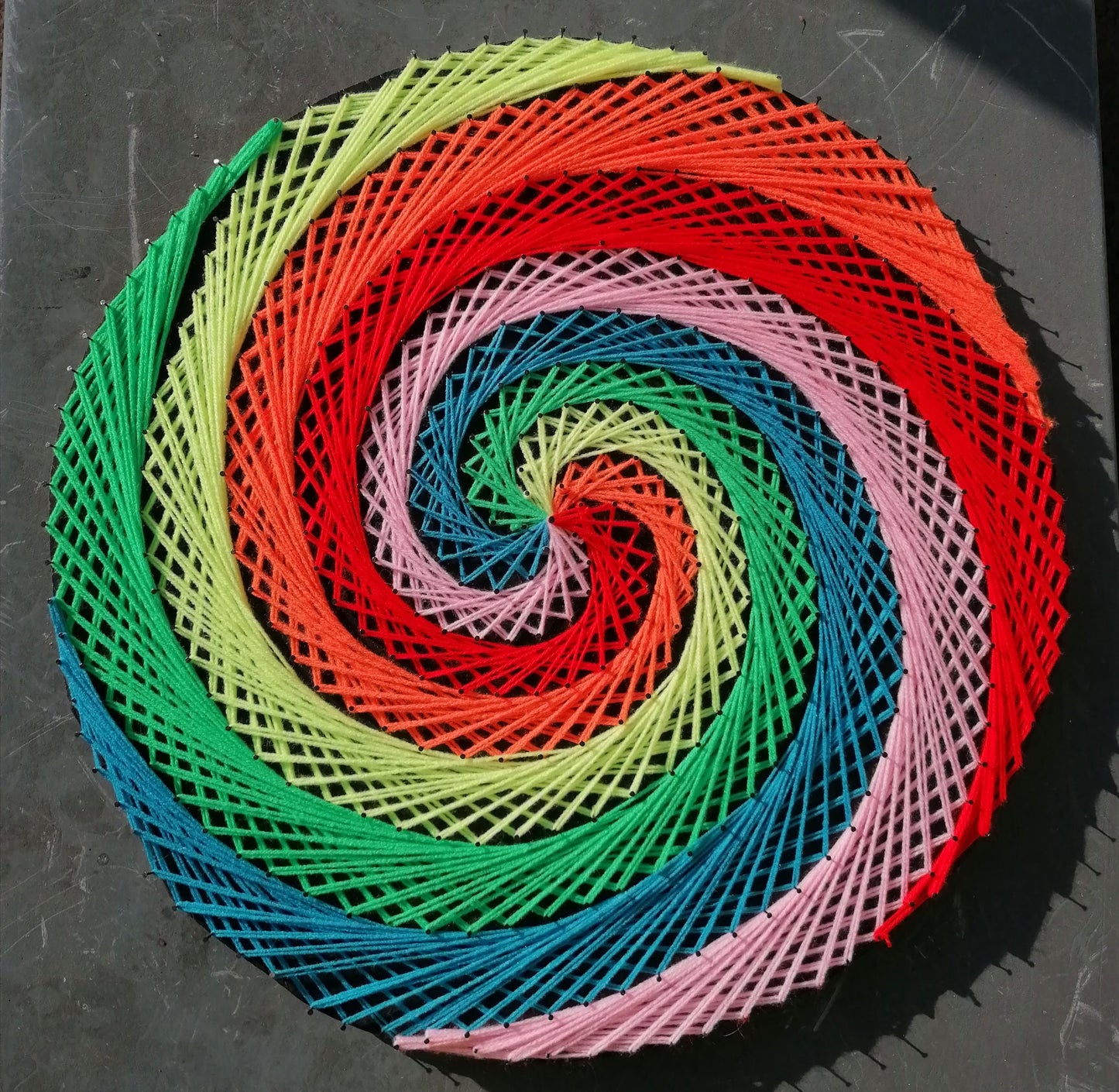 Colorful spiral pattern made of interwoven strings on a dark surface