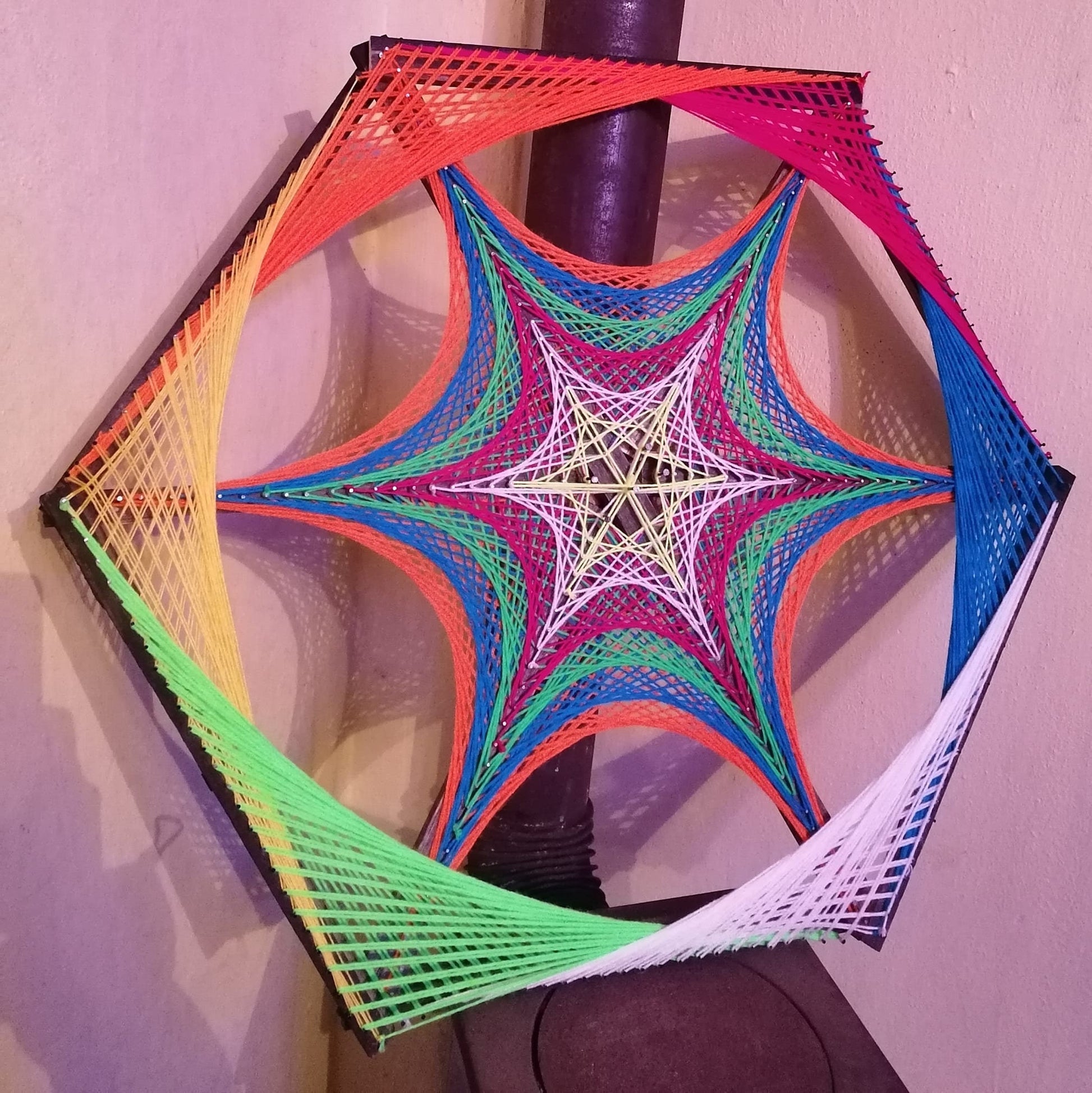 Colorful hexagon string art with star-shaped geometry, handmade UV-reactive threads arranged on nails, photographed on black background with vibrant neon colors