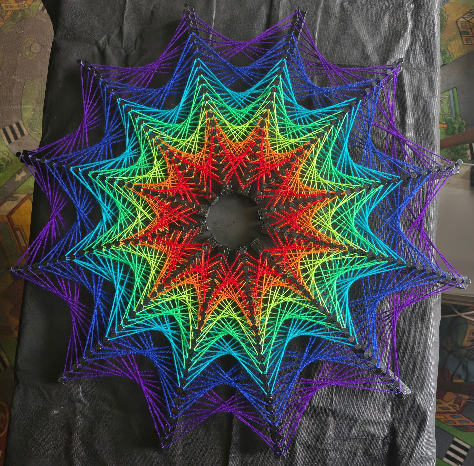 Cosmic Stargate handmade string art photographed on table with black background, star-shaped geometric pattern with vivid contrasting colors, modern psychedelic wall art by Psybell