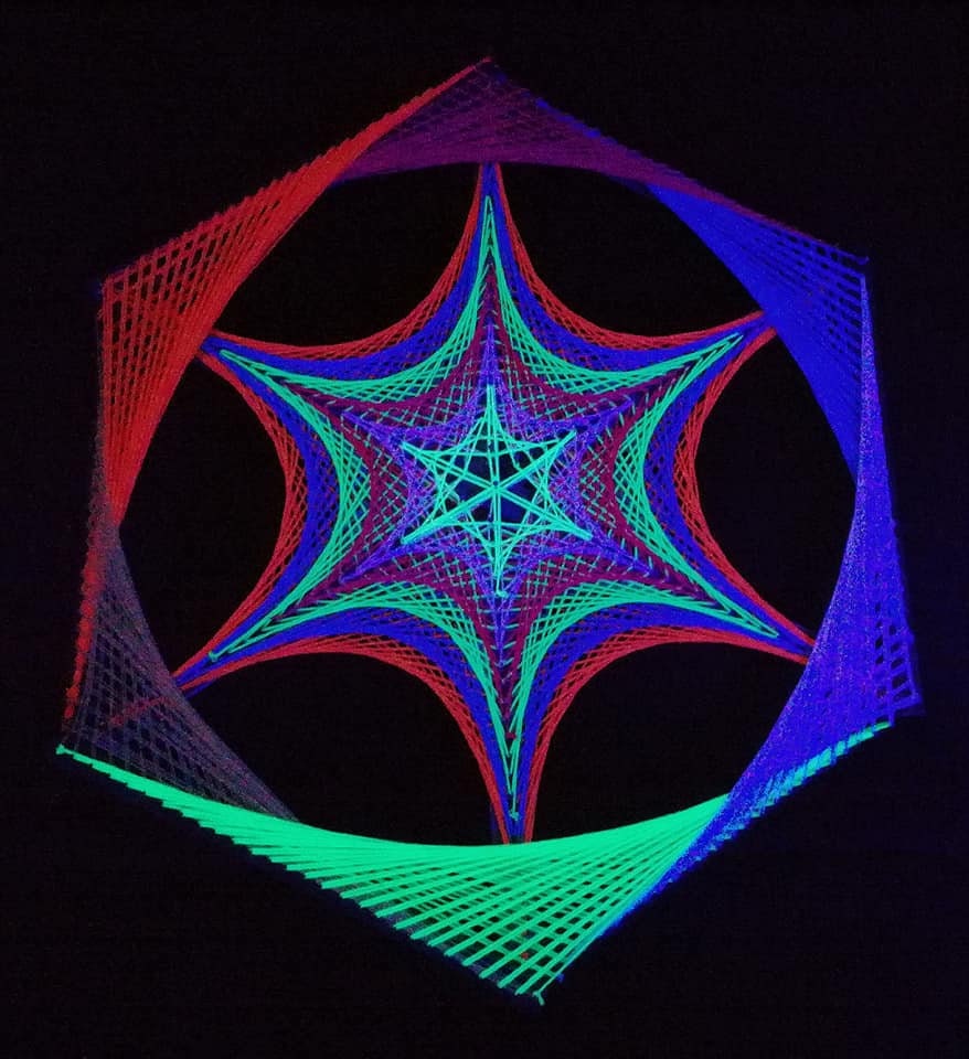 Handmade hexagon string art featuring layered star geometry, neon and UV-reactive threads glowing against dark background