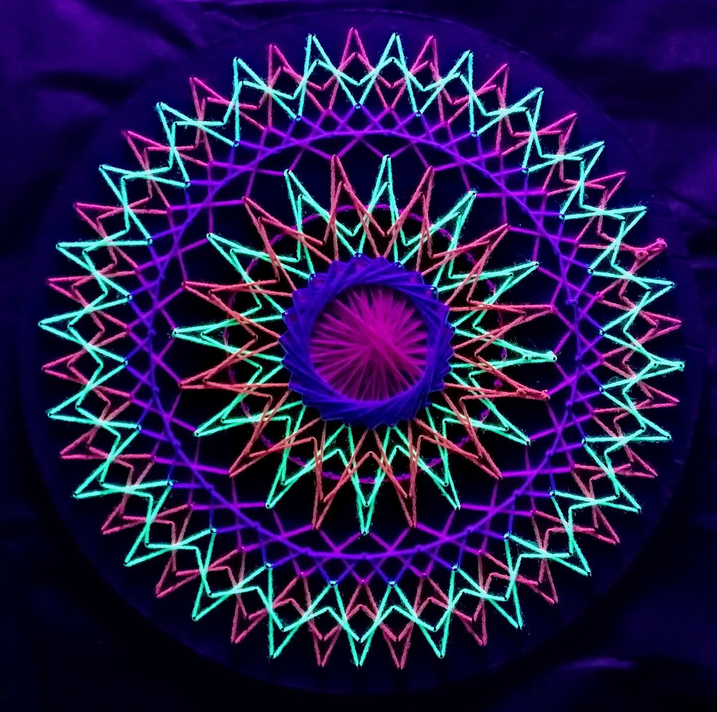 handmade UV reactive string art mandala with symetrical circular geometry, neon colors, made from cotton threads, by Psybell