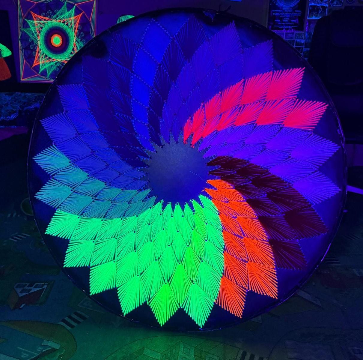 UV reactive handmade string art circle with symmetrical geometric pattern, rainbow colors design, made from synthetic acrylic threads on MDF wood board, by Psybell, from Slovakia
