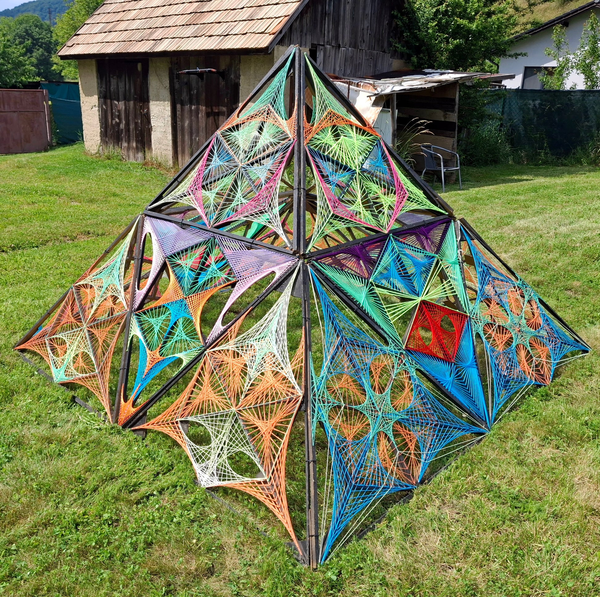 Psybell Pyramid 3D string art sculpture photographed in daylight, handmade geometric pyramid made of threads and wooden structure, contemporary string art object