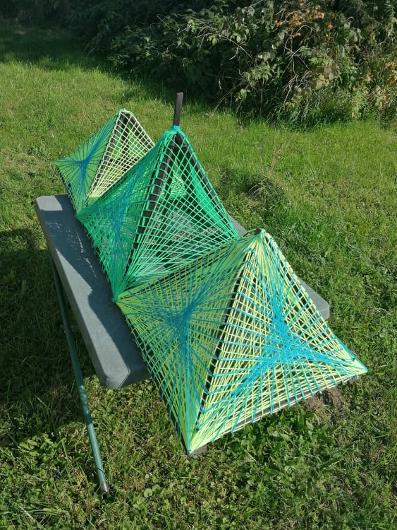 Handmade triple green string art pyramid installation, geometric 3D pyramids woven with neon green and blue threads on outdoor table