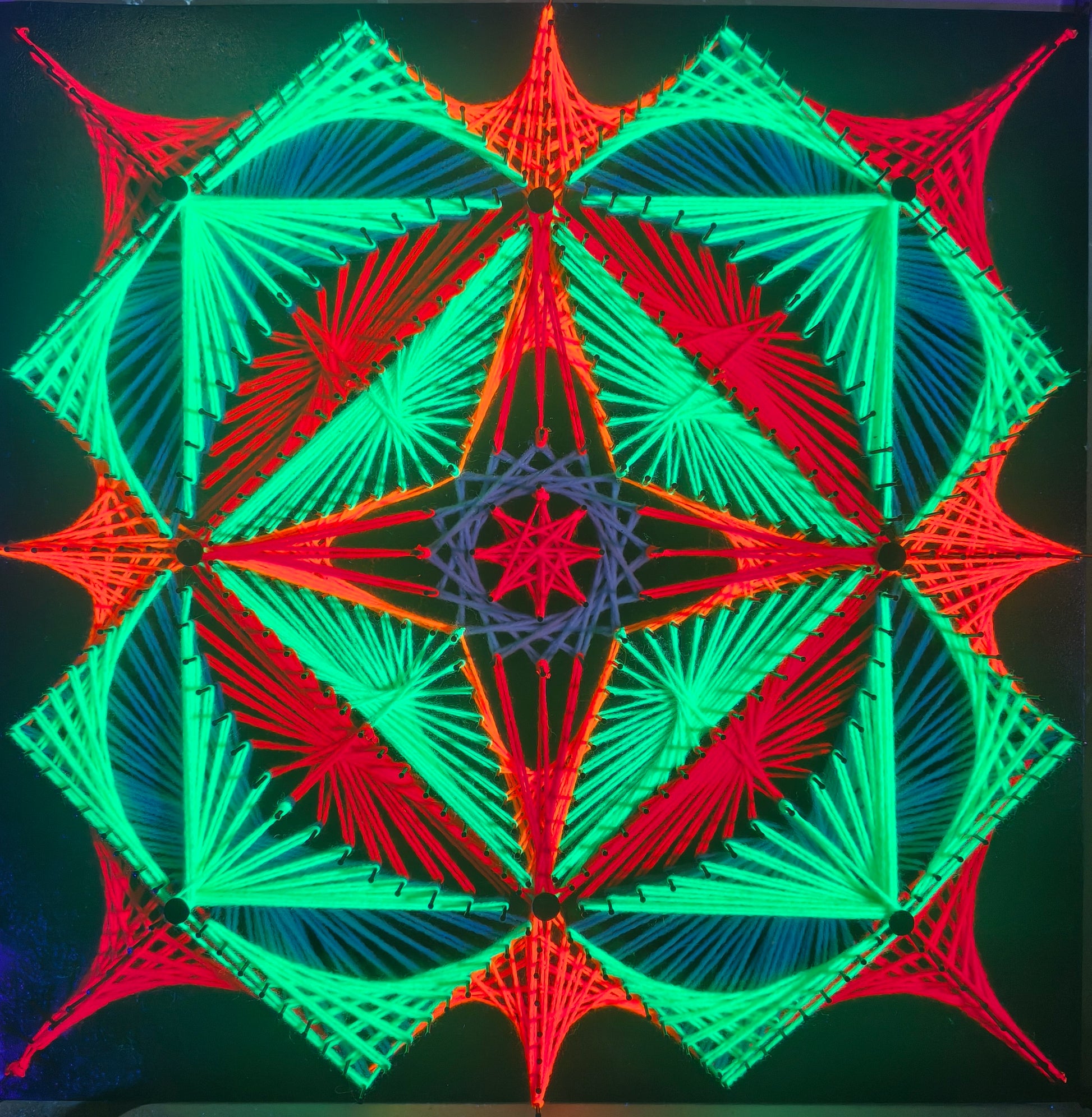 handmade UV reactive square string art with symmetrical geometric pattern, neon green and red colors, glowing under ultraviolet light, by Psybell, from Slovakia