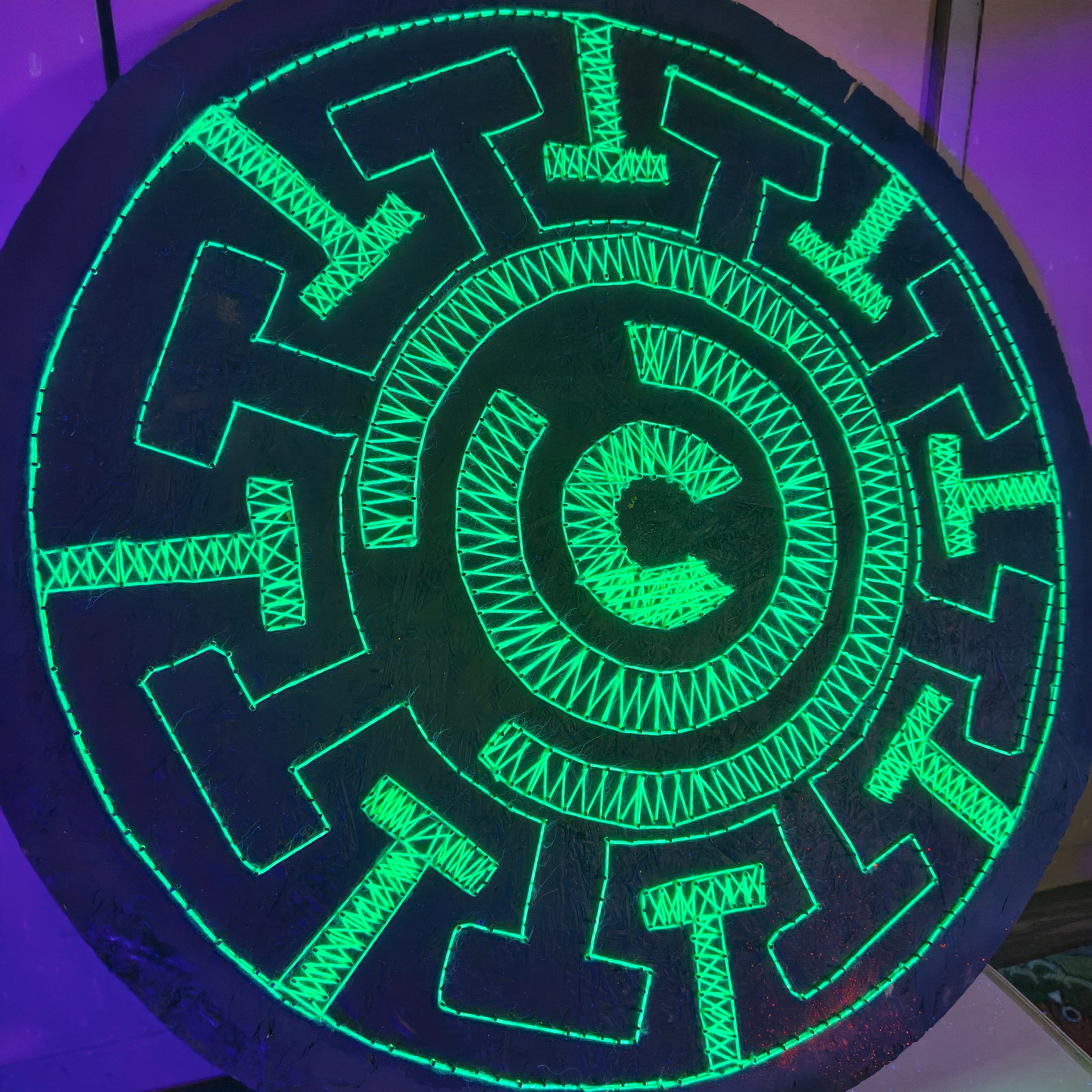 UV string art Labyrinth mandala handmade geometric wall art glowing under blacklight on dark wooden background