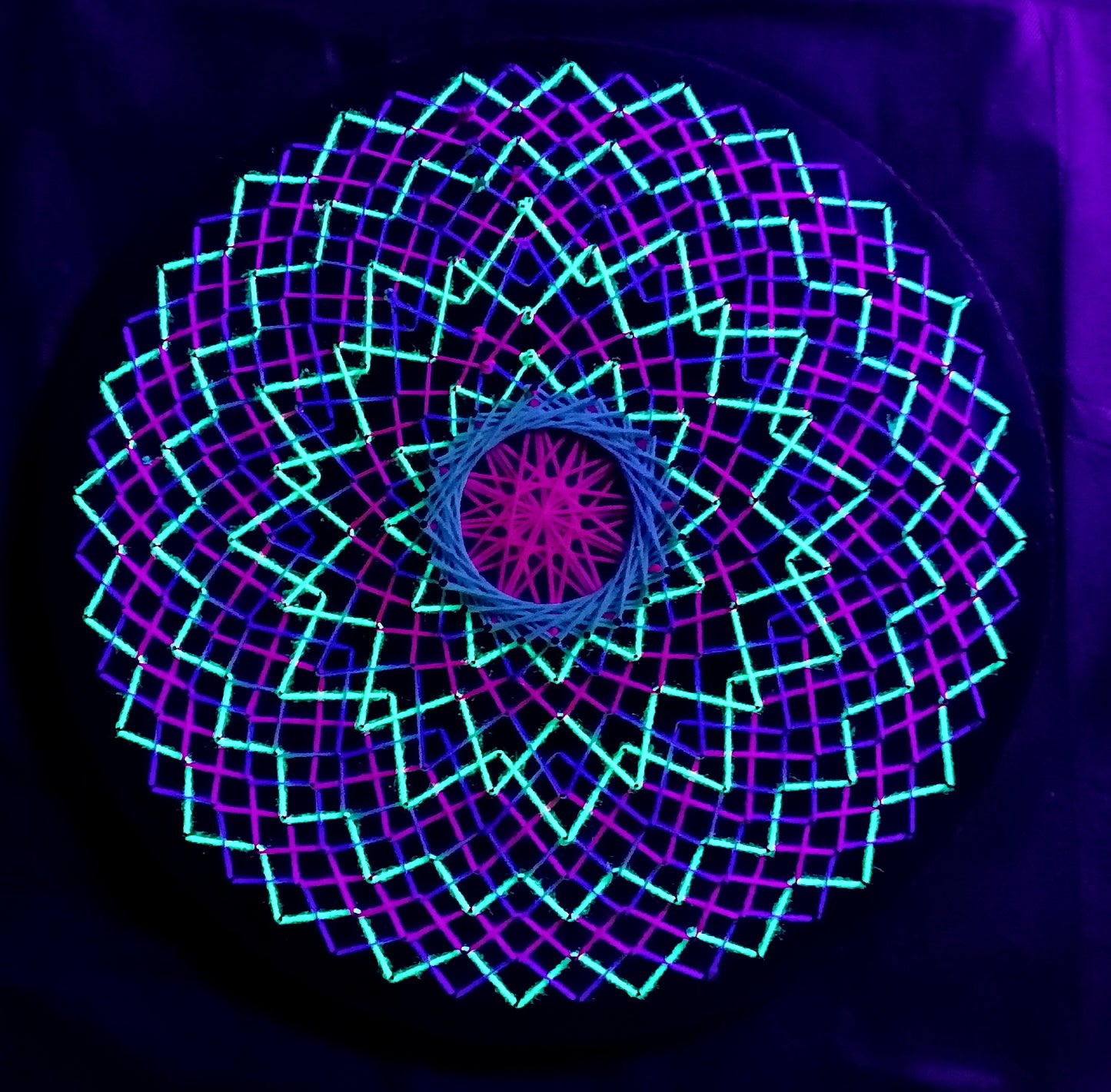 handmade UV reactive string art mandala with symmetrical circular geometry, neon colors, made from cotton threads, by Psybell