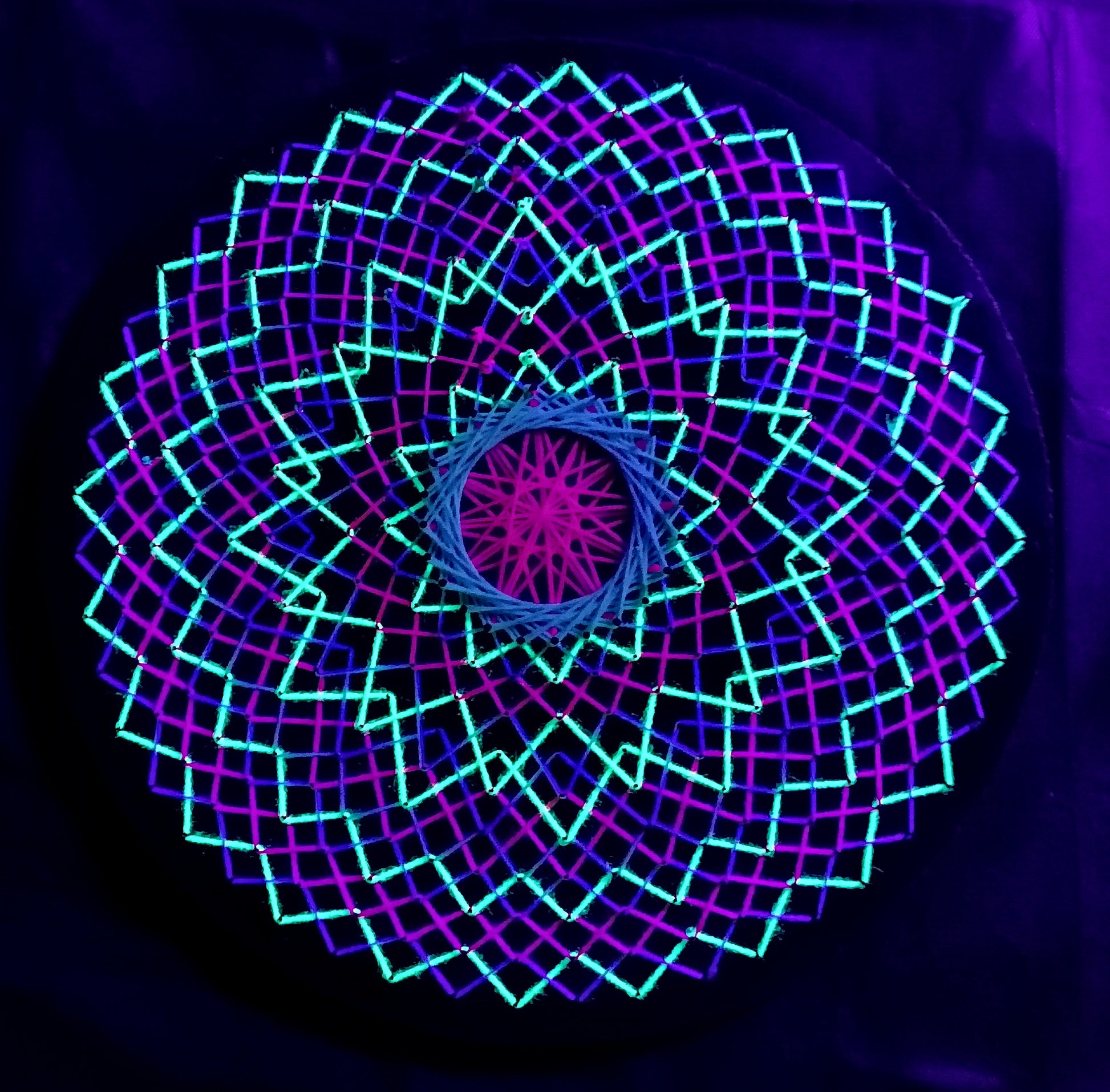 handmade UV reactive string art mandala with symmetrical circular geometry, neon colors, made from cotton threads, by Psybell
