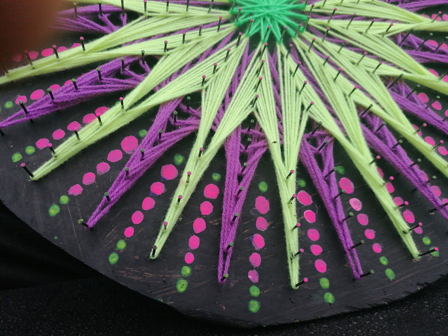 Macro detail of geometric string art jellyfish pattern by Psybell showing fluorescent threads and dotted mandala elements on wooden board