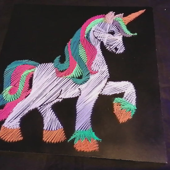 handmade UV reactive unicorn string art made from neon cotton threads, glowing under ultraviolet light, geometric silhouette with rainbow mane and tail on black MDF board by Psybell