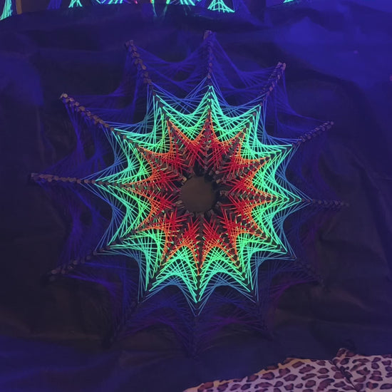 Detail view of Cosmic Stargate string art, star geometry woven with colorful threads on black surface, high contrast handmade artwork