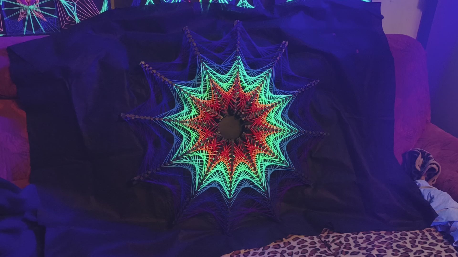 Detail view of Cosmic Stargate string art, star geometry woven with colorful threads on black surface, high contrast handmade artwork