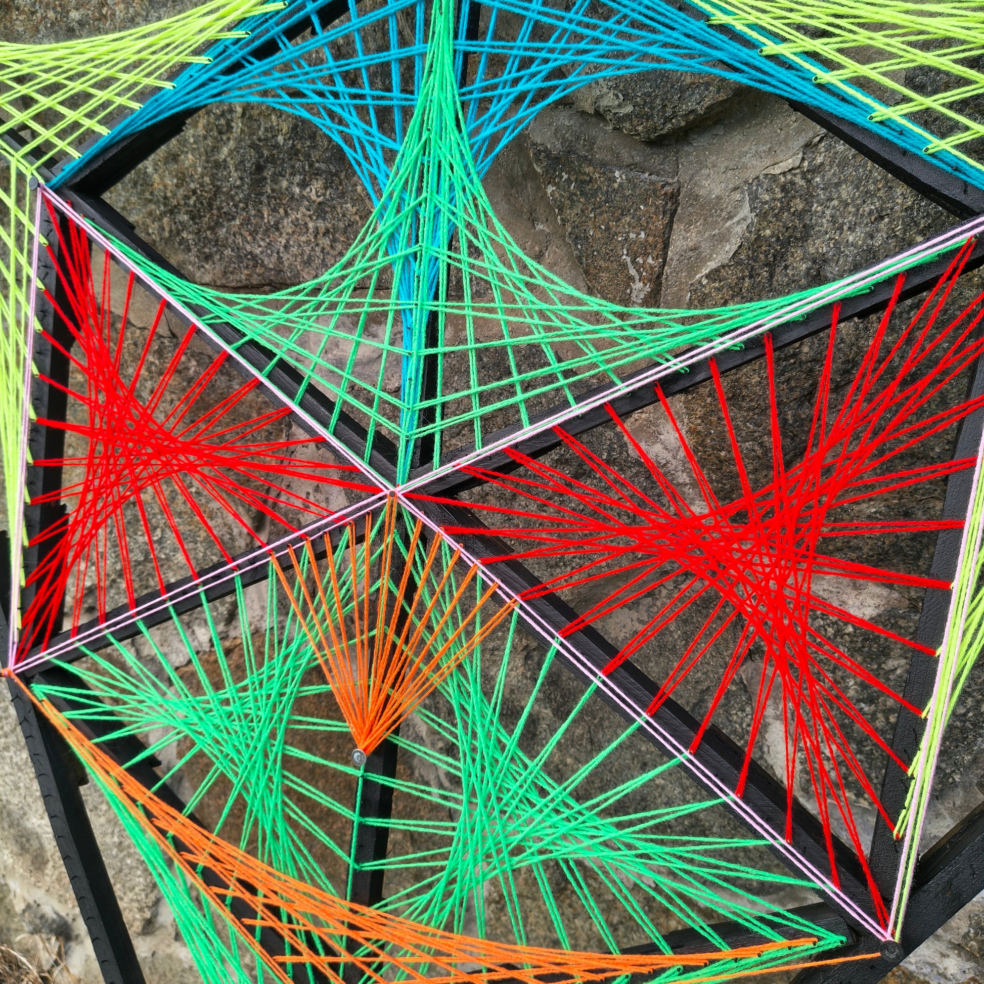 Detail of geometric string art Alien Hunter by Psybell showing colorful thread pattern on stone background