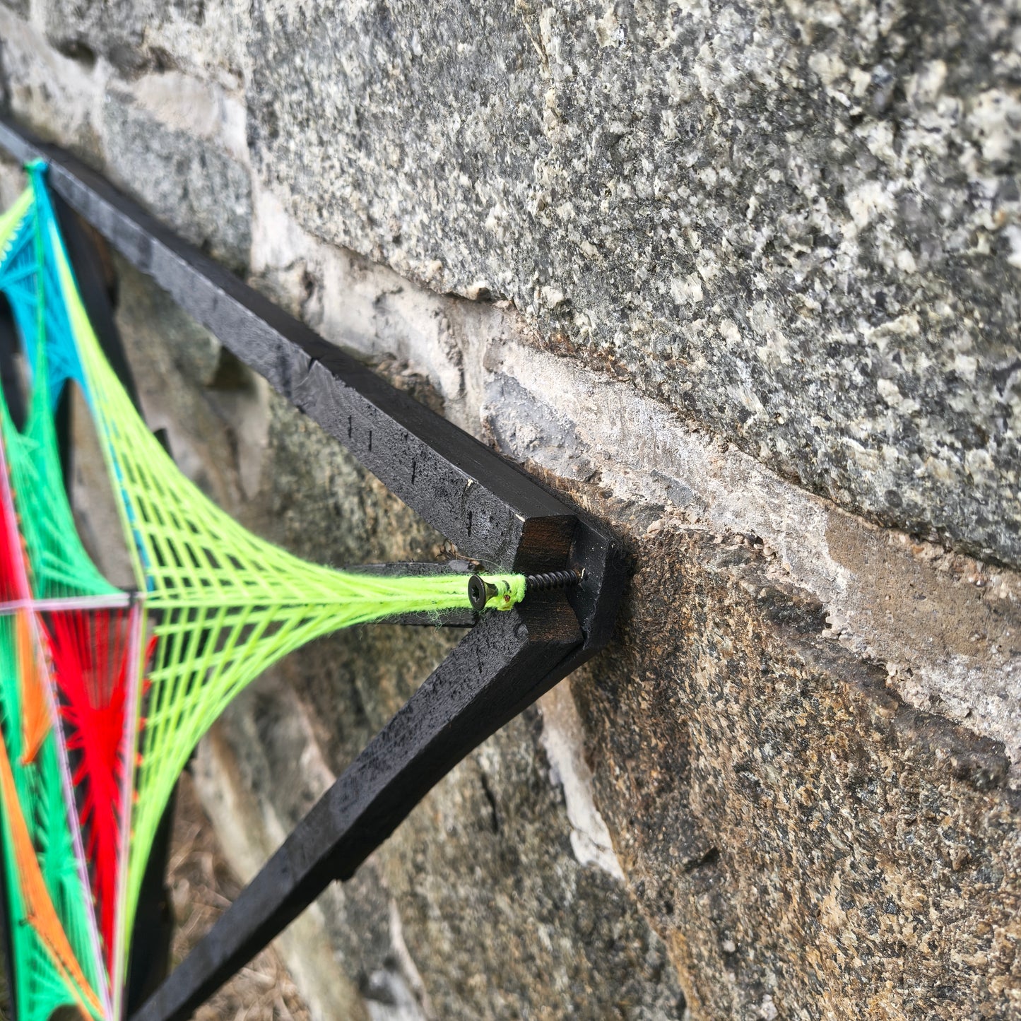 Detail of Alien Hunter string art frame by Psybell mounted on a stone wall