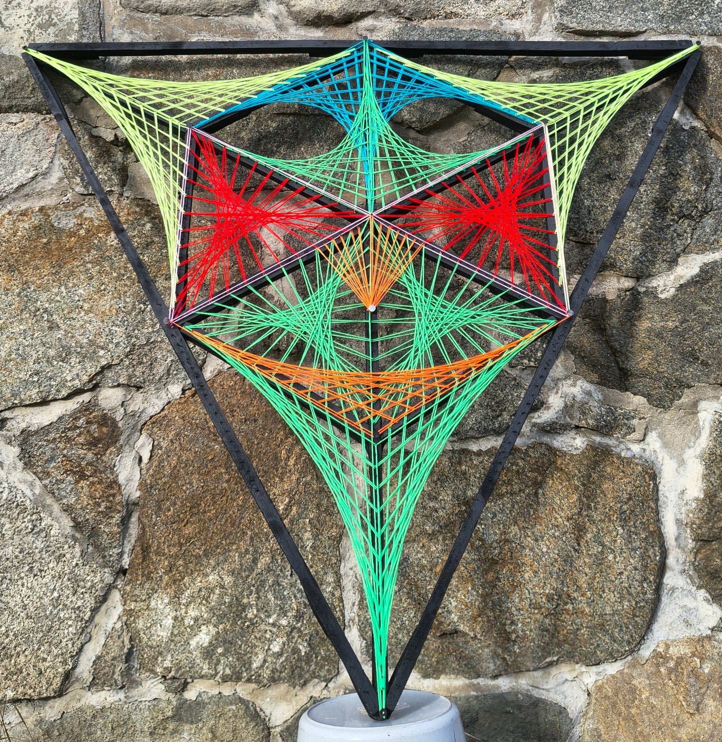 Alien Hunter geometric string art wall sculpture by Psybell displayed against a stone wall