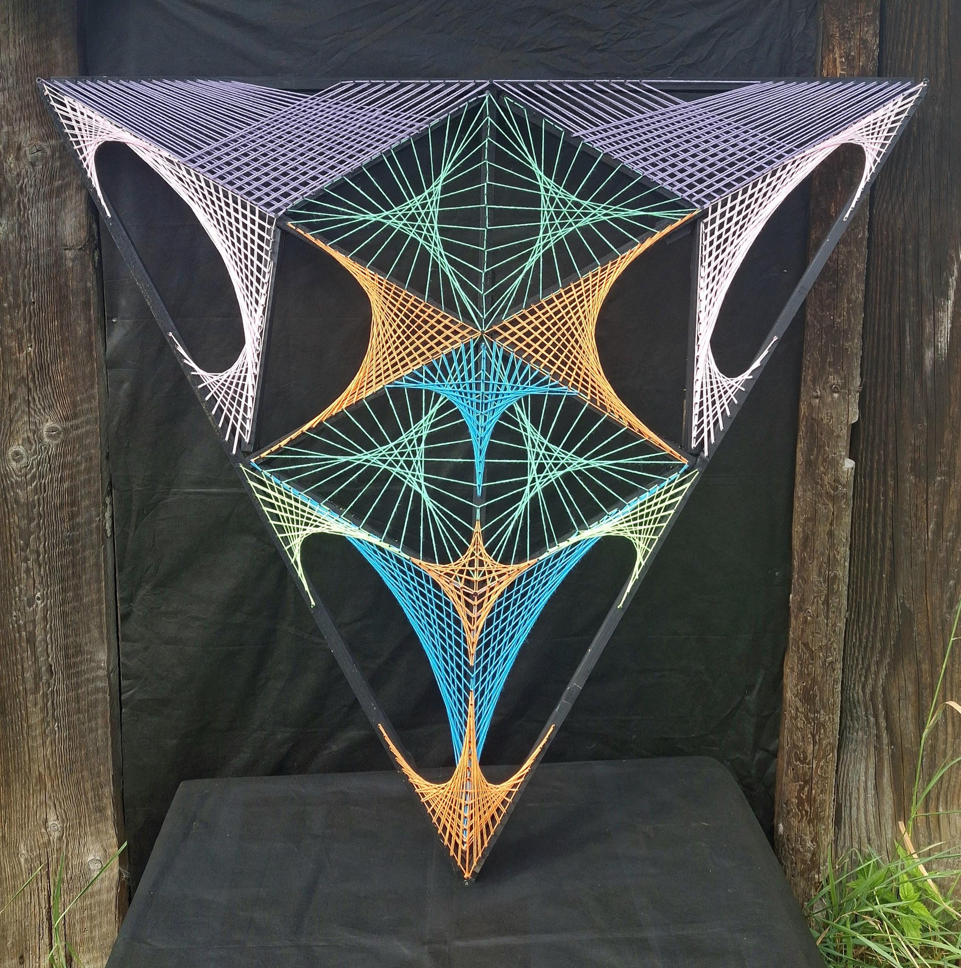 Geometric string art sculpture Aliens Gate by Psybell displayed outdoors on a table with wooden background