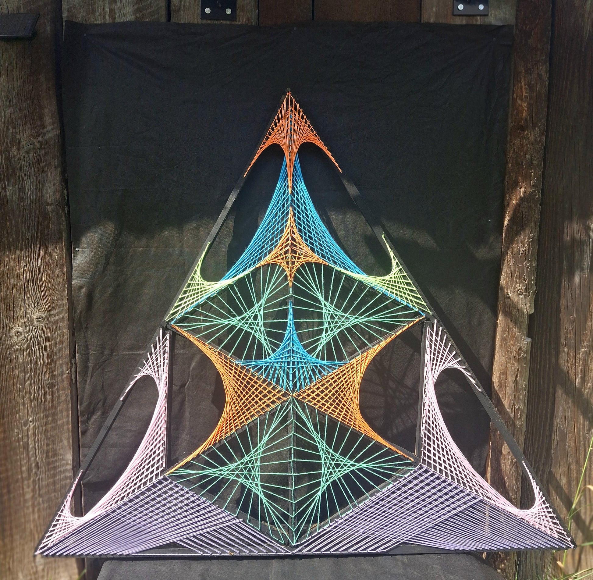 Geometric string art wall sculpture Aliens Gate by Psybell displayed outdoors against dark fabric background