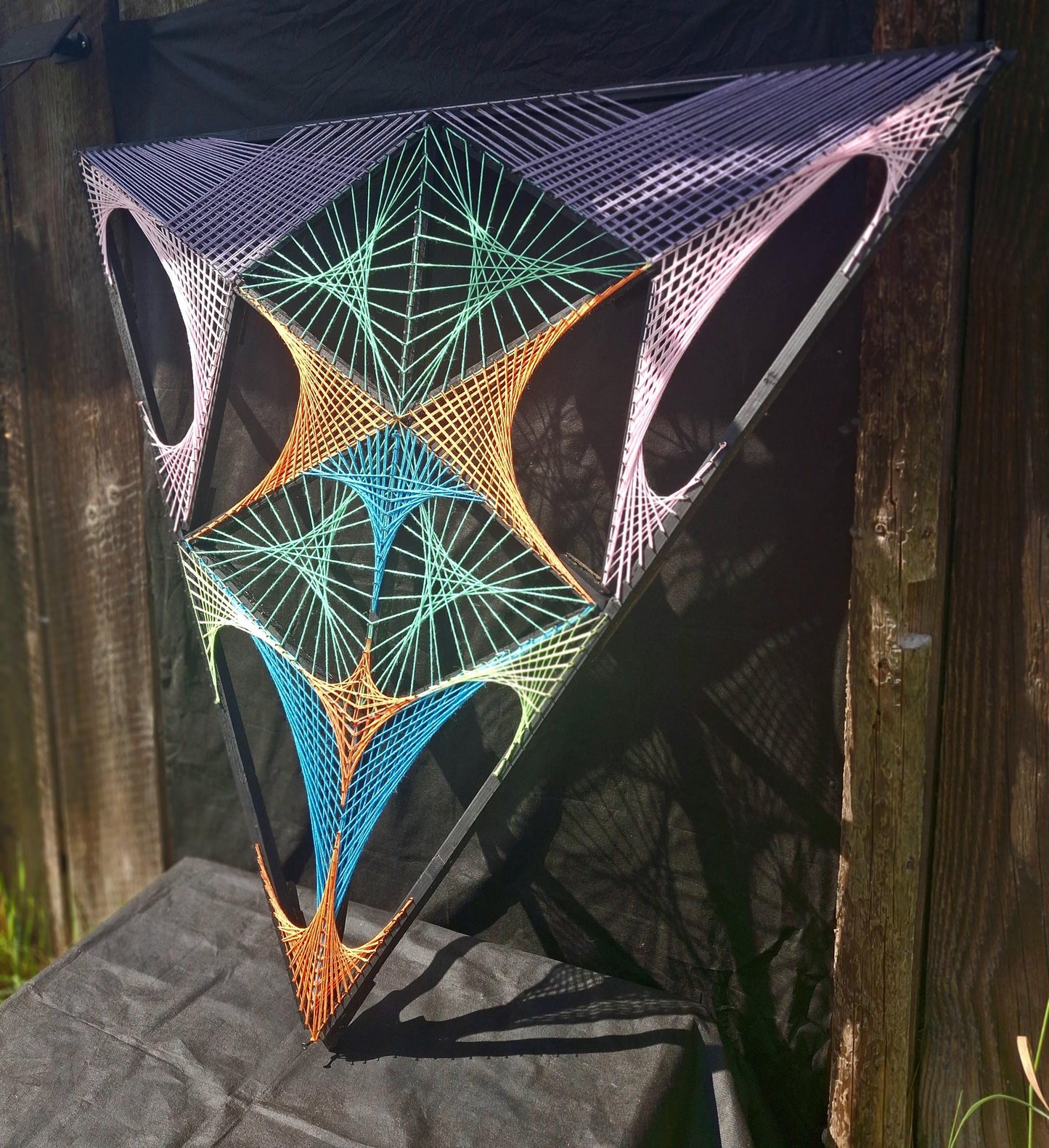 UV reactive geometric string art sculpture Aliens Gate by Psybell displayed outdoors on a wooden surface