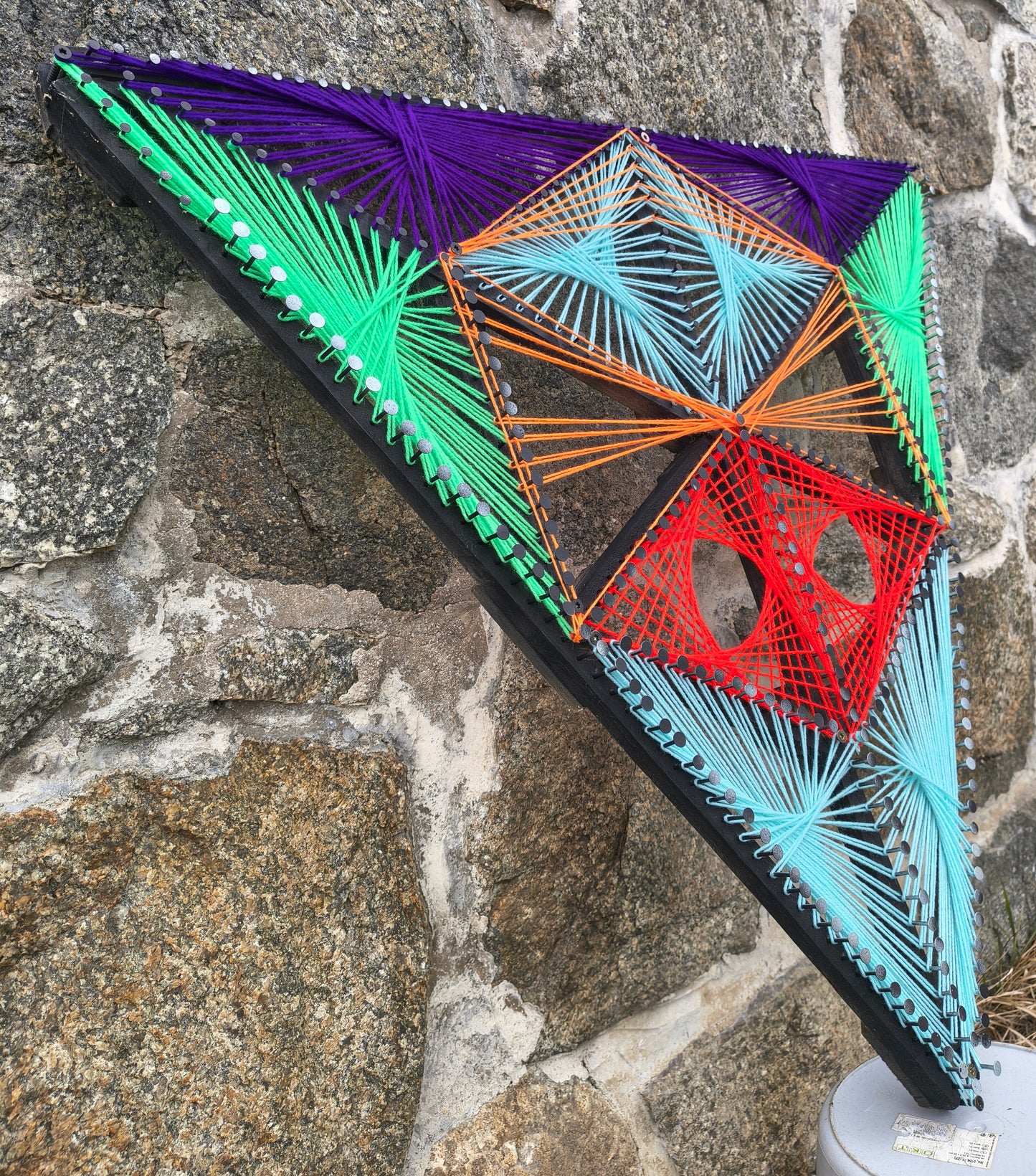 Aliens Sentinel Mini geometric string art sculpture by Psybell viewed at an angle against a stone wall