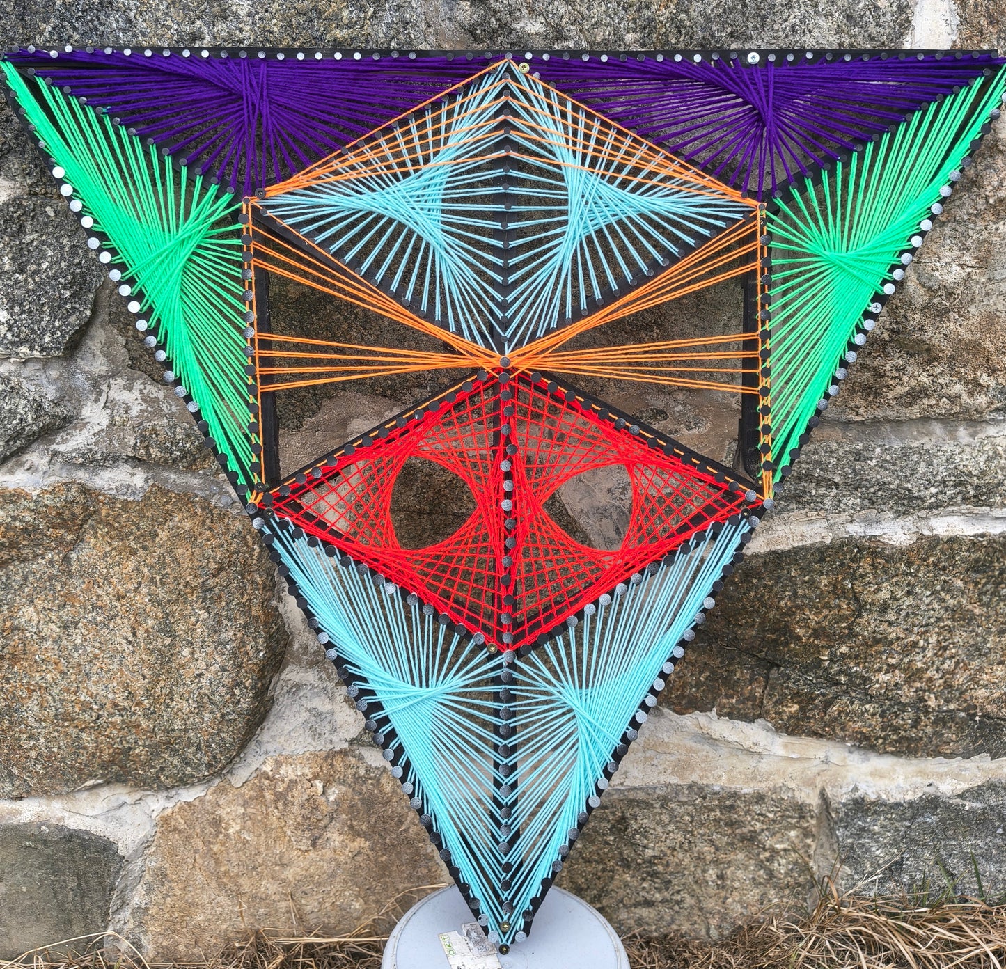 Aliens Sentinel Mini geometric string art wall sculpture by Psybell displayed against a stone wall