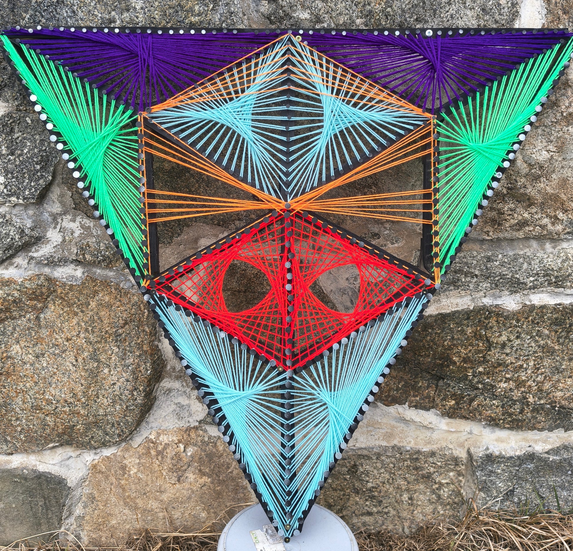 Aliens Sentinel Mini geometric string art wall sculpture by Psybell displayed against a stone wall