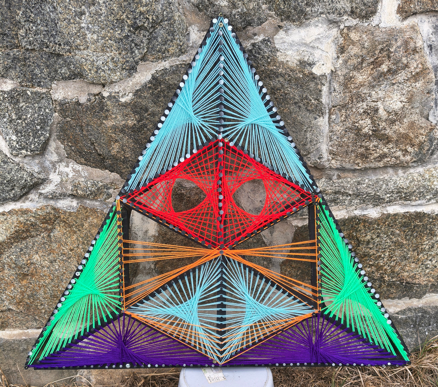 Geometric string art wall artwork Aliens Sentinel Mini by Psybell displayed against a stone wall