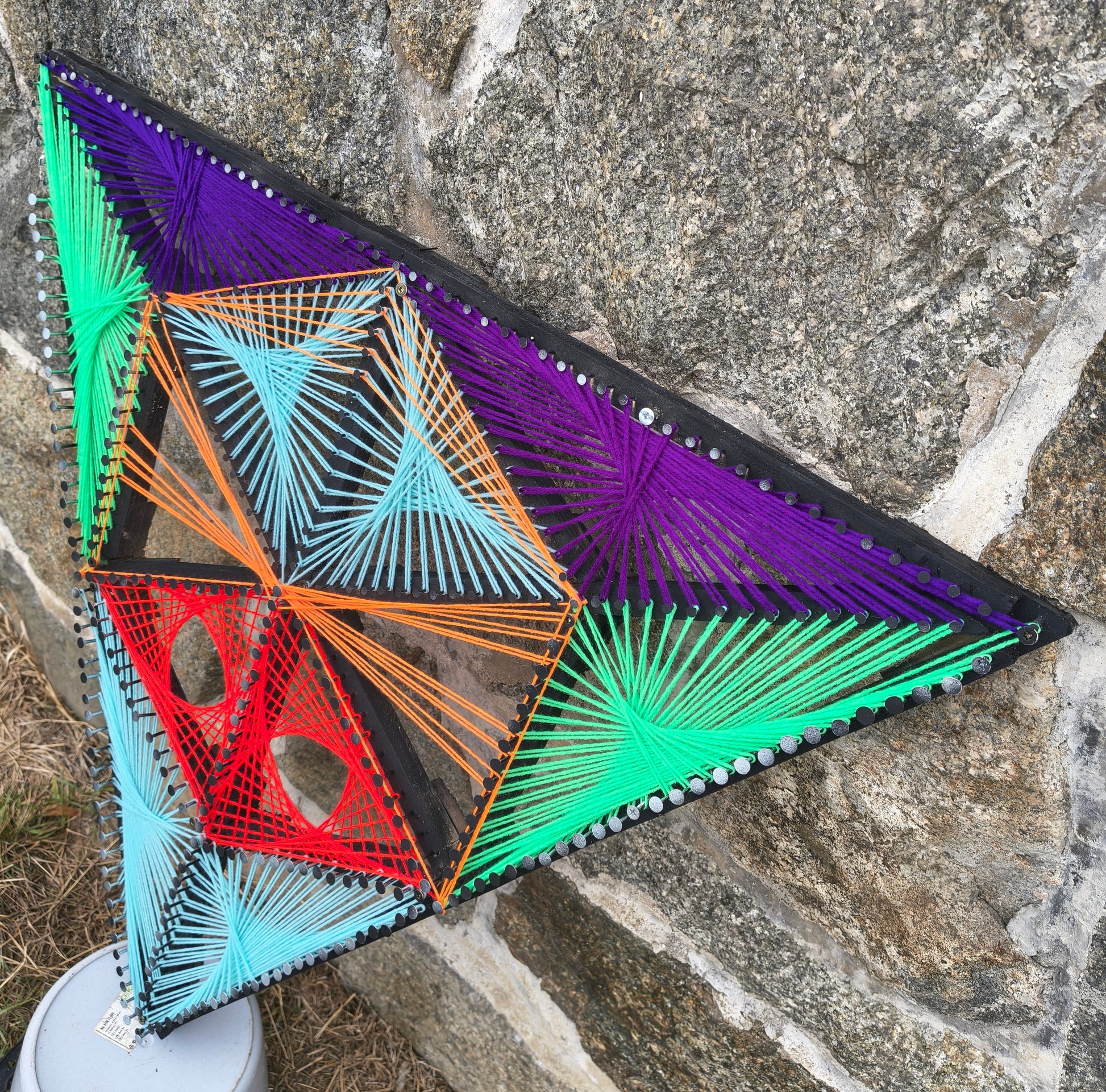 Aliens Sentinel Mini triangular geometric string art sculpture by Psybell displayed against a stone wall