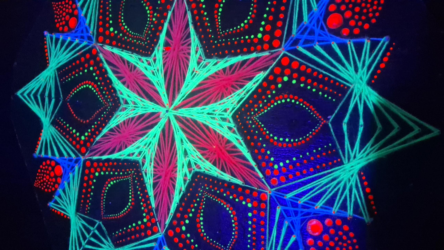 Macro detail of UV reactive geometric string art mandala “Blooming Anise” by Psybell glowing under blacklight showing handmade threads and dotted mandala pattern