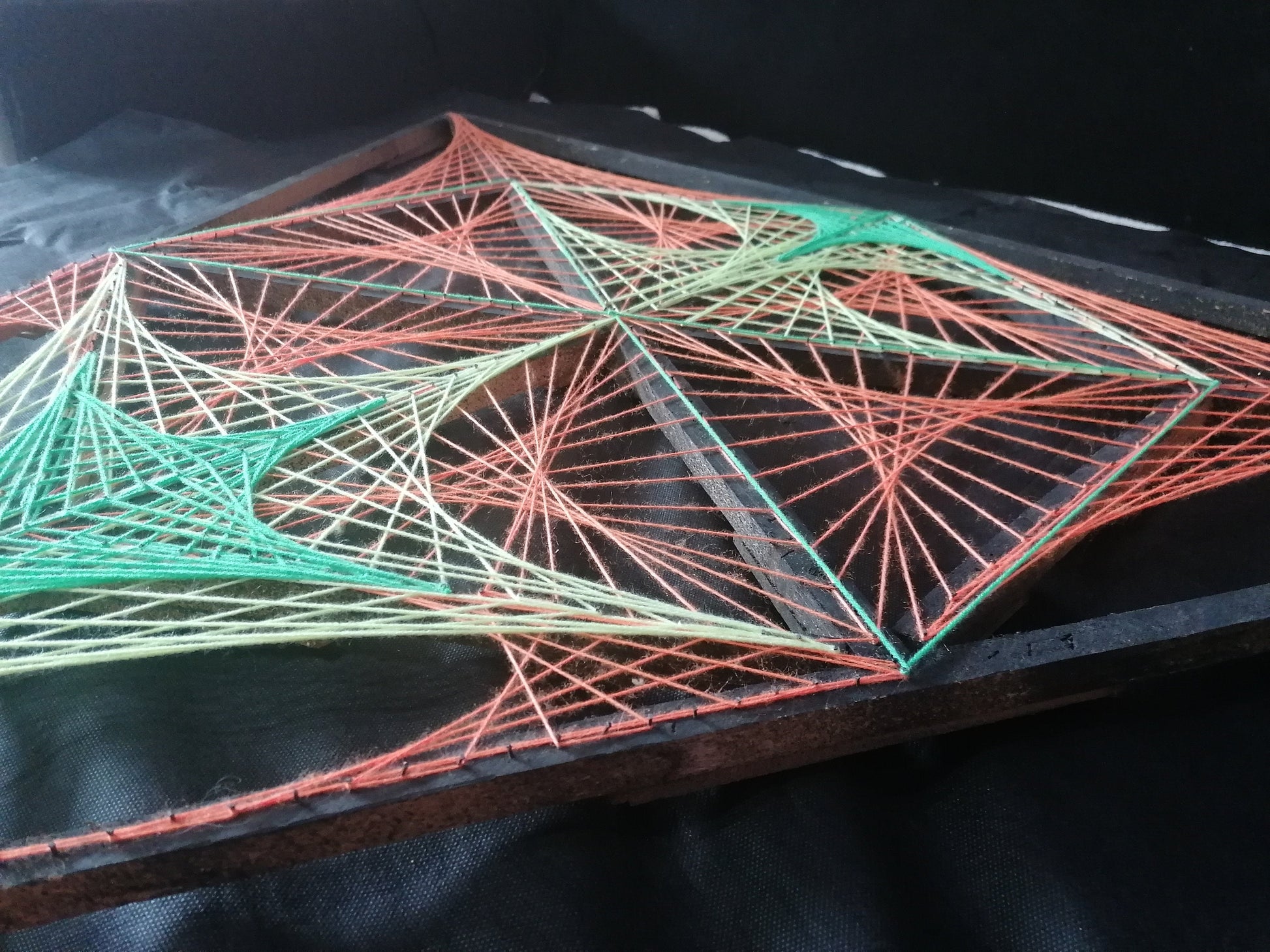 Detail of geometric string art installation by Psybell showing colorful intersecting threads on dark background