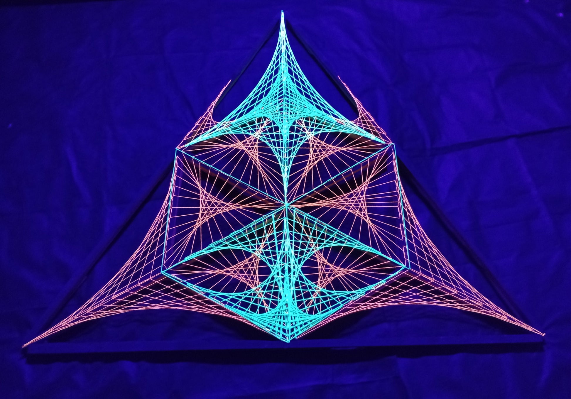 Front view of UV reactive geometric string art installation by Psybell glowing under purple UV lighting