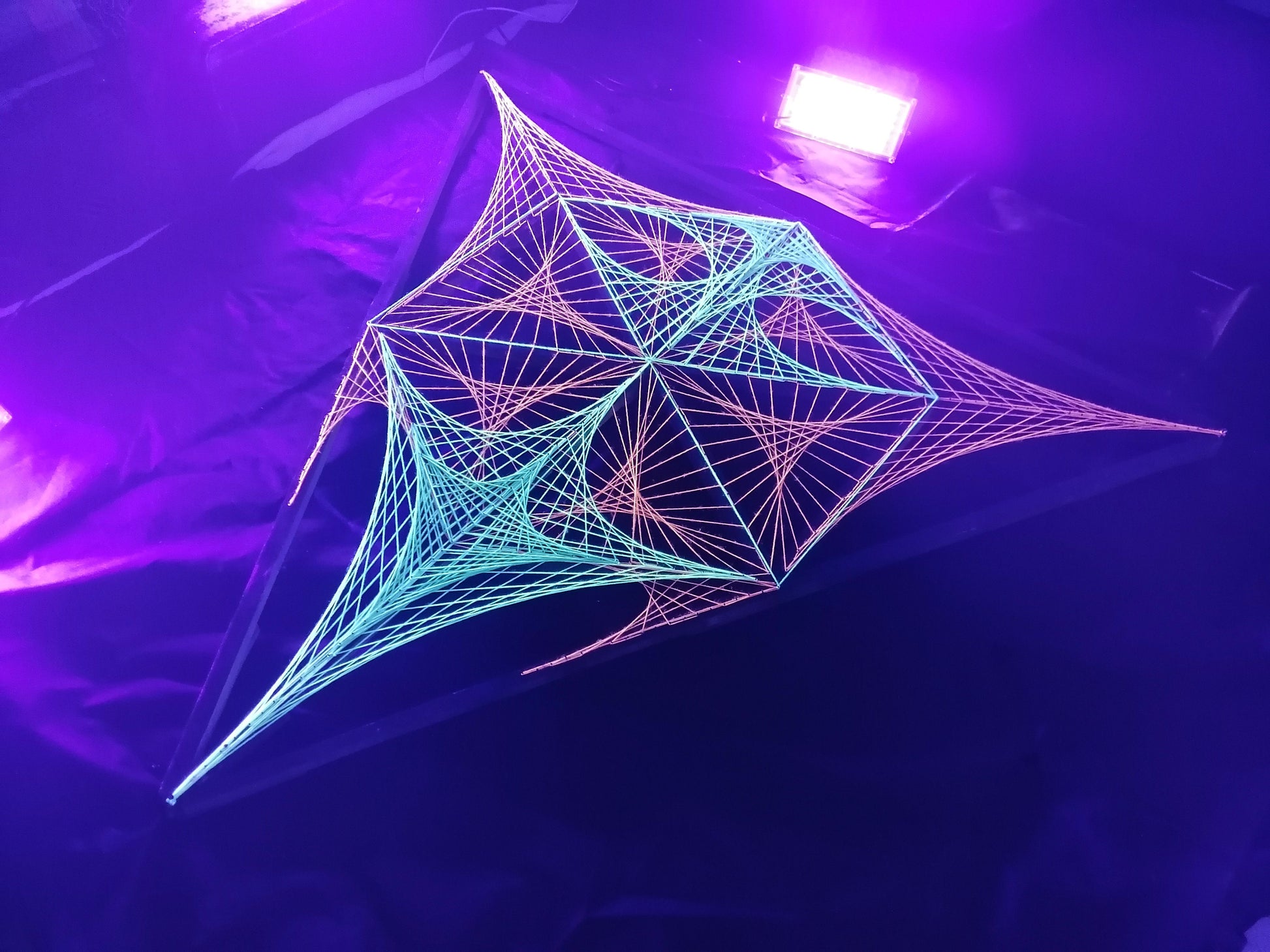 UV reactive geometric string art installation by Psybell glowing under purple stage lighting