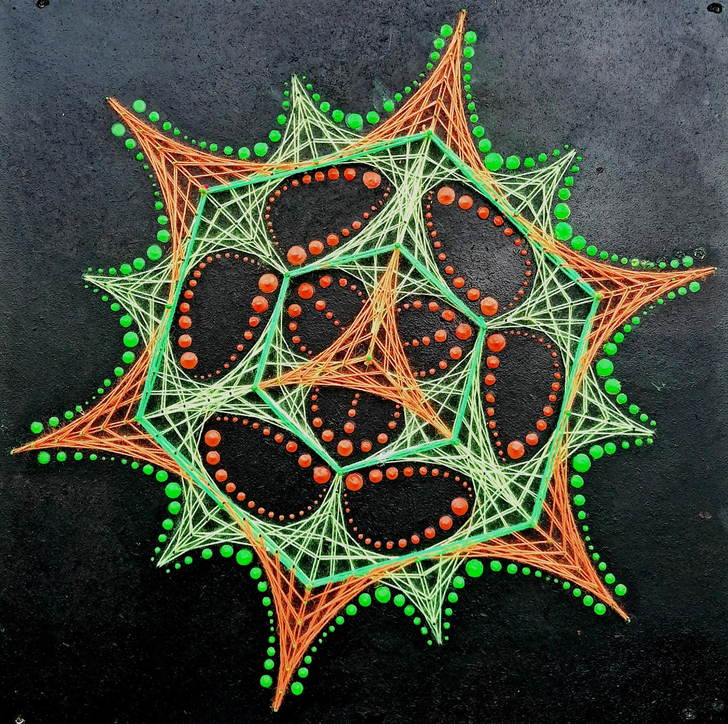 Front view of UV reactive dotted mandala string art “Transformer” by Psybell on dark textured background